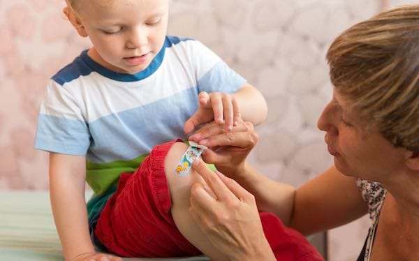 Woman putting plaster on child's knee